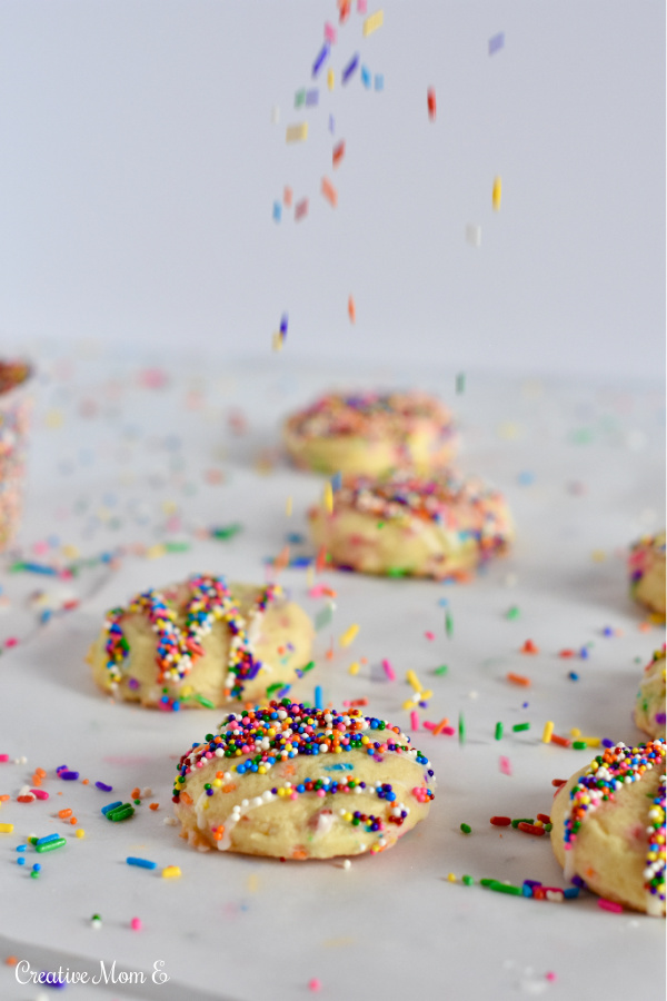 Sprinkle sugar cookies sitting on counter with sprinkles falling on cookies.