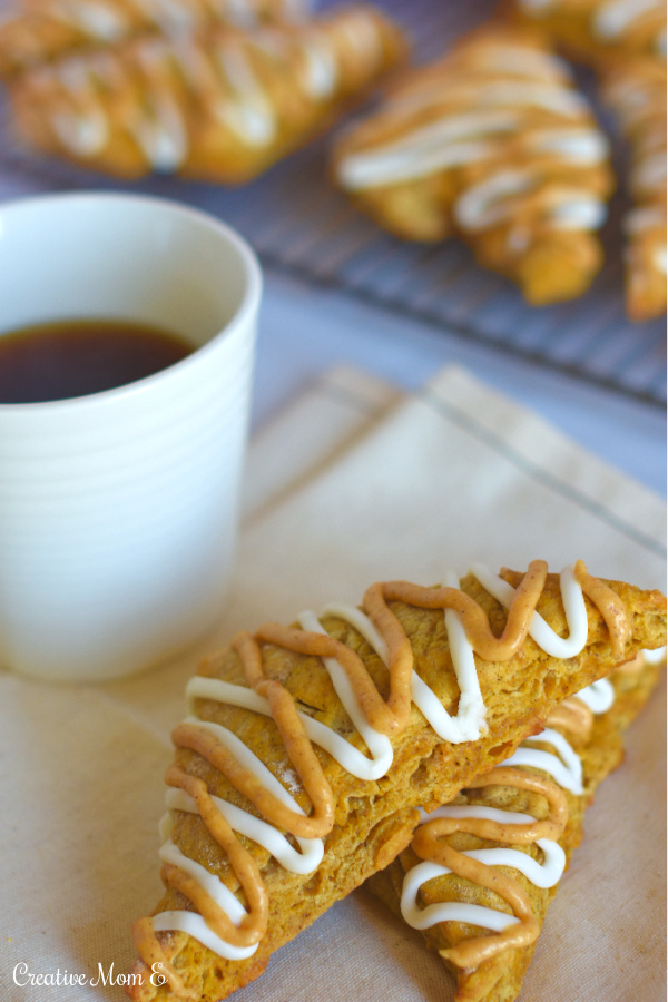 Classic pumpkin spice scones on a napkin with a cup of coffee with a cooling rack filled with more pumpkin scones in the background.