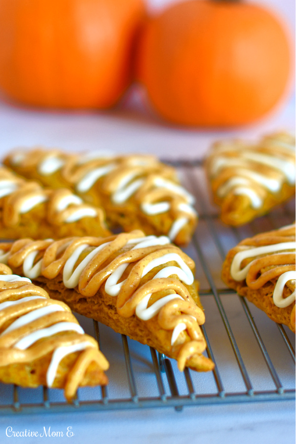 Classic pumpkin spice scones on a cooling rack topped with icing and pumpkins sitting in the background. 