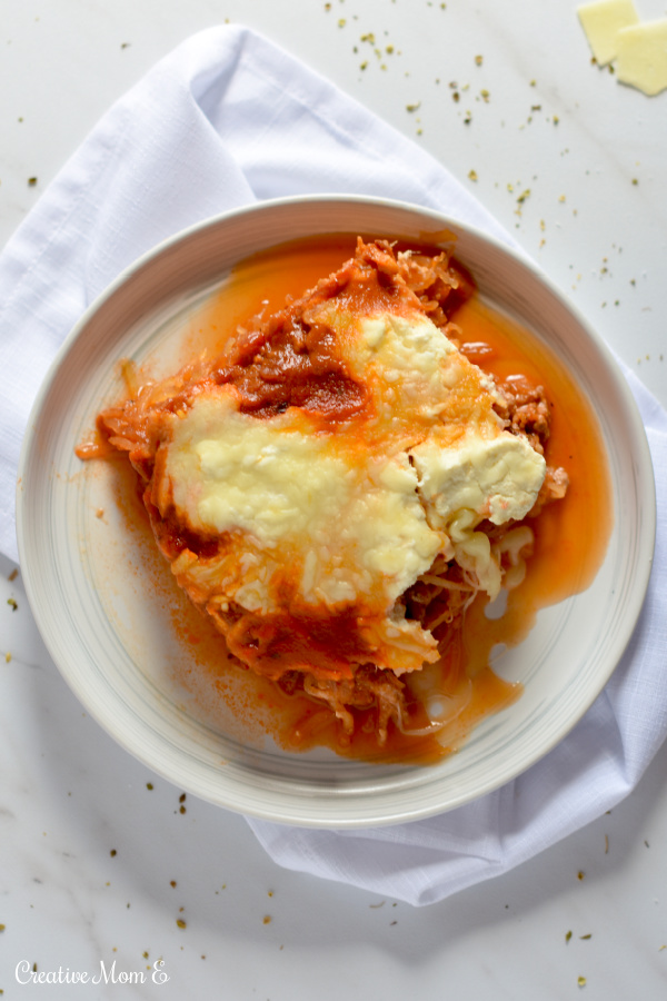 A serving of lasagna on a round white plate sitting on top of a white napkin .