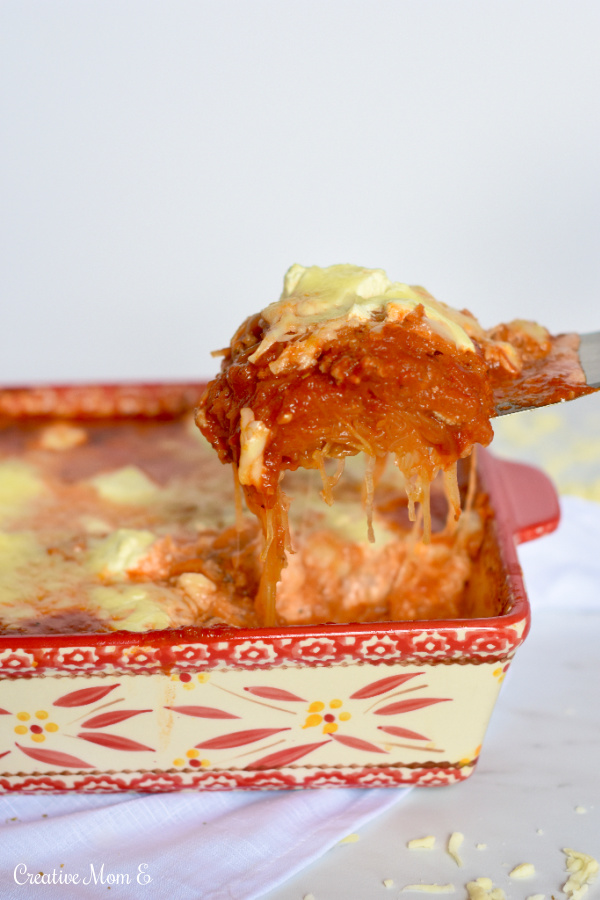 Scooping out a serving of lasagna out of the red baking dish which is sitting on a white napkin sprinkled with cheese. 