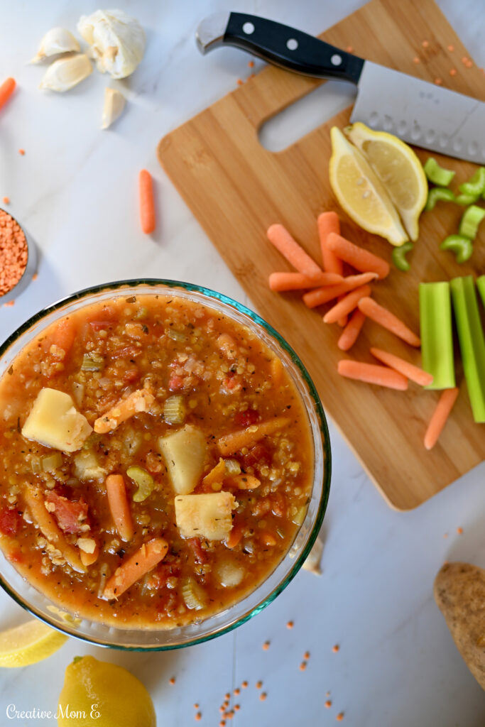 Bowl with lentil soup next to a cutting board with carrots, lemon, celery and a knife
