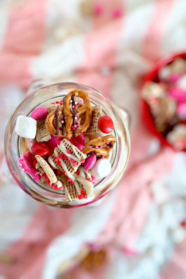 Clear jar filled with chocolate covered Chex and pretzels with sprinkles and marshmallows and m&ms. 