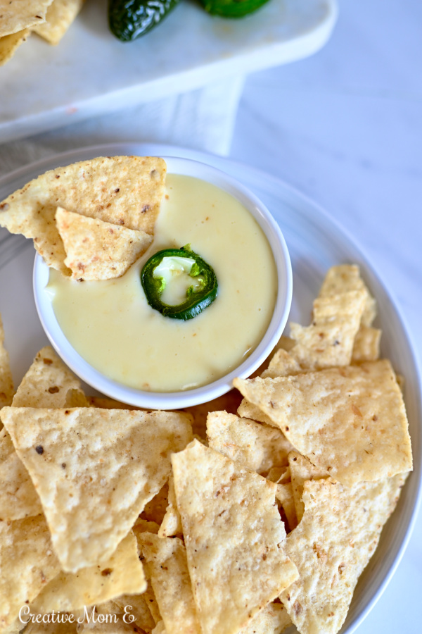 Single serving of cheese dip in a white bowl with tortilla chips. 
