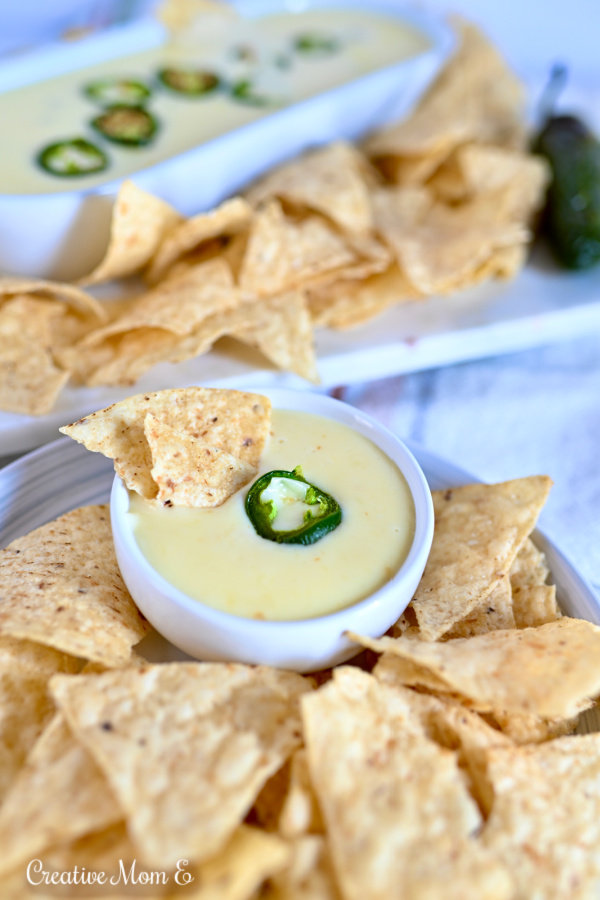 Spicy white cheese dip with a tortilla chip in it in a white bowl. 