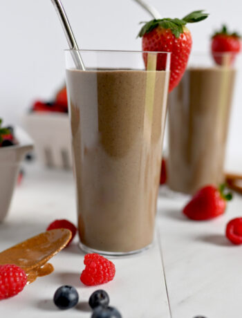 clear glass with a brown smoothie surrounded by raspberries and strawberries