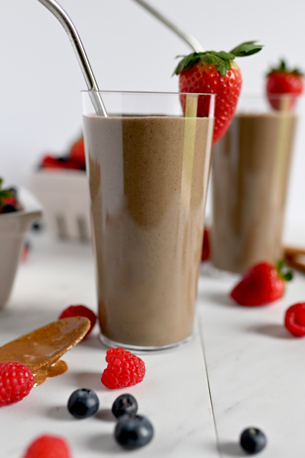 clear glass with a brown smoothie surrounded by raspberries and strawberries