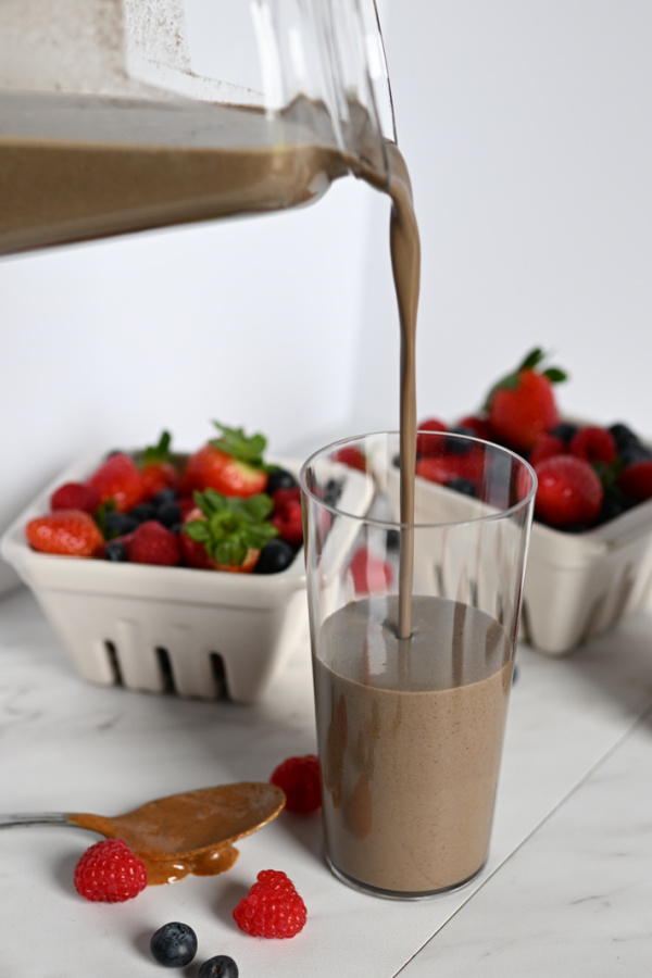 Clear pitcher filling up a glass with healthy triple berry smoothie surrounded by berry dishes