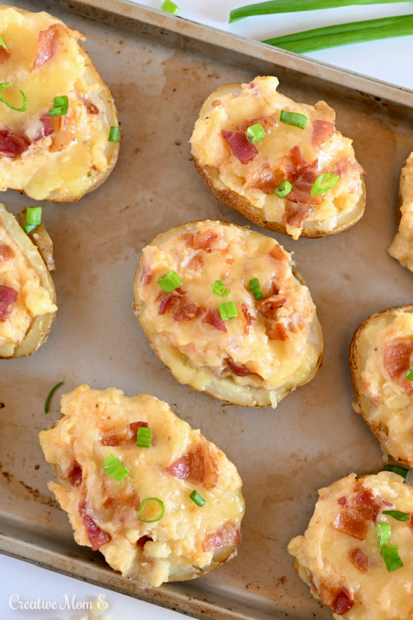 Baked potatoes on a baking sheet topped with bacon and chives.