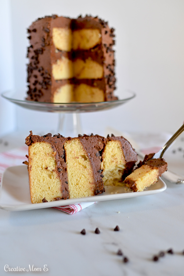 Slice of yellow cake with chocolate frosting on a white plate and a bite missing. 