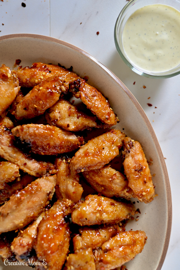 Sweet and tangy chicken wings on a tan plate with a side of ranch.
