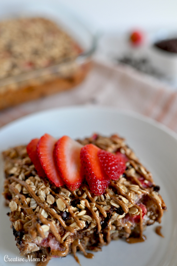 Baked oatmeal square on a white plate topped with almond butter and sliced strawberries. 