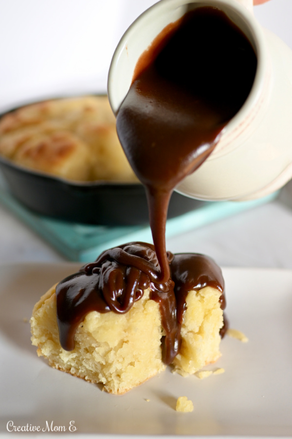 Chocolate gravy being poured over a buttered biscuit on a white plate. 