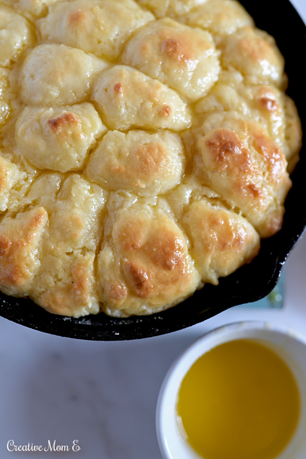Cast iron skillet filled with buttery biscuits next to a side of butter.