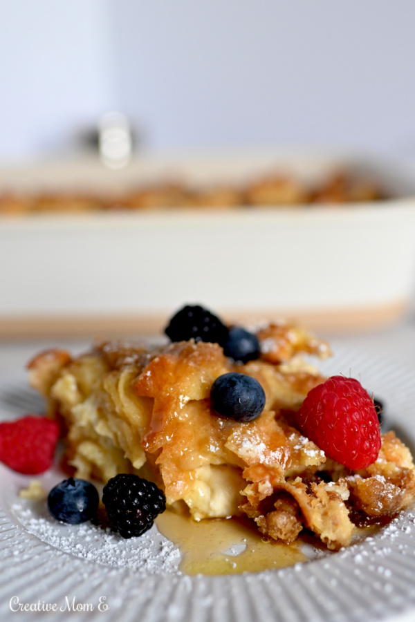 Overnight French toast casserole with fresh berries and powdered sugar on a white plate. 