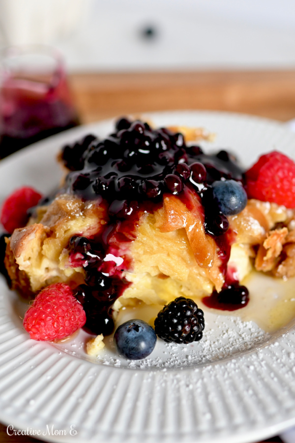 Cream Cheese Overnight French Toast on a white plate drizzled with blueberry syrup.