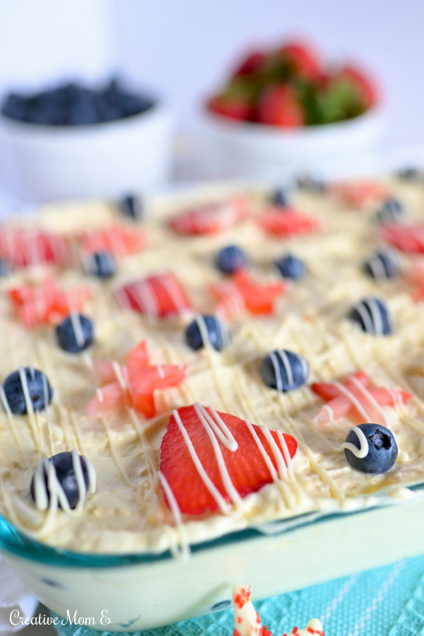 Icebox cake in a clear dish with white chocolate drizzled over strawberries and blueberries.