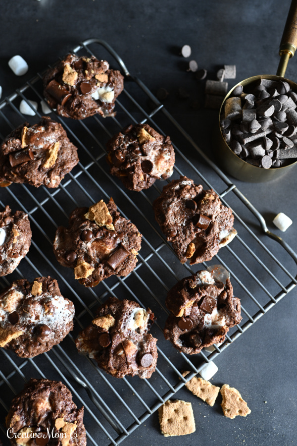 S'mores cookies on a cookie cooling rack next to a cup of chocolate chips 