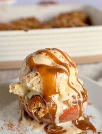 Baked peach crumble on a white place with a heaping scoop of vanilla ice cream and a caramel drizzle.