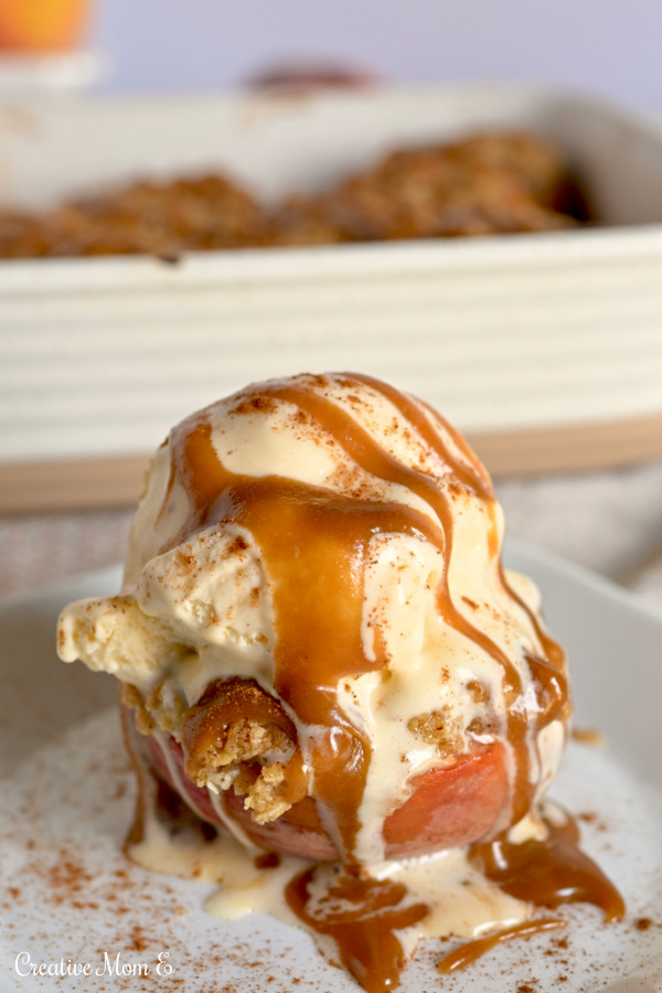 Baked peach crumble on a white place with a heaping scoop of vanilla ice cream and a caramel drizzle.