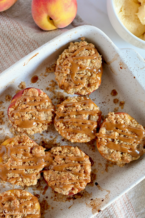 A pan filled with individual baked peach crumble drizzled with caramel sauce. 