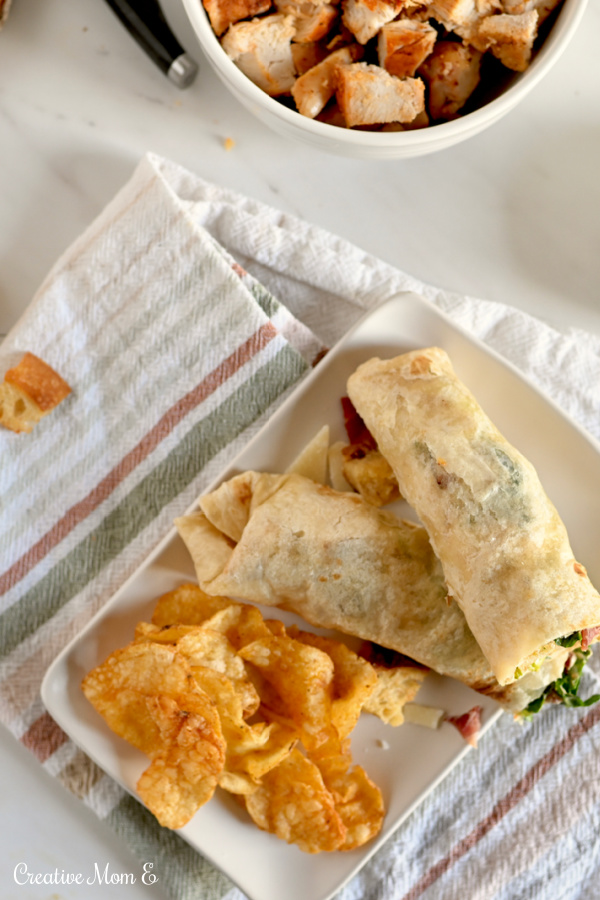 Two bacon caesar wraps on a white rectangle plate over a striped towel.