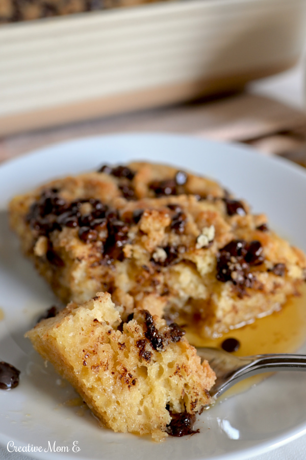 A fork full of chocolate chip pancake casserole drizzled with maple syrup on a white plate. 