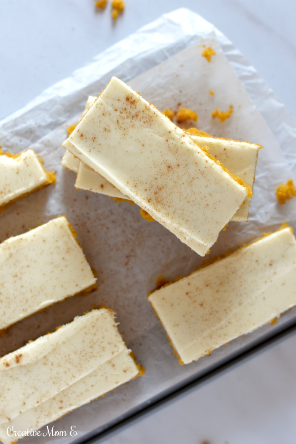 Stacks of amazing pumpkin bars on parchment paper dusted with cinnamon. 