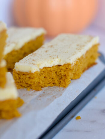 A bite taken out of a cookie sheet pumpkin bar with cream cheese frosting.