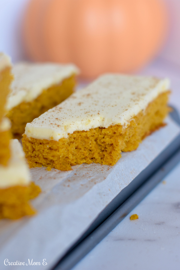 A bite taken out of a cookie sheet pumpkin bar with cream cheese frosting.