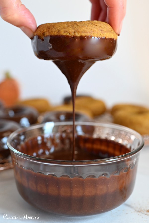 Dipped pumpkin cake donut in a bowl of Mexican chocolate glaze.