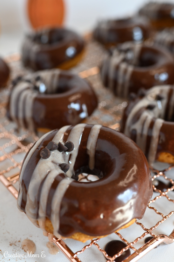 Pumpkin Cake Donuts with a chocolate glaze on a copper cooling rack.