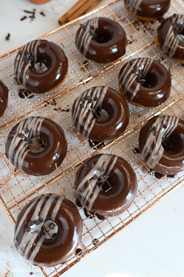 A dozen chocolate pumpkin fall baked donuts on a copper cooling rack. 