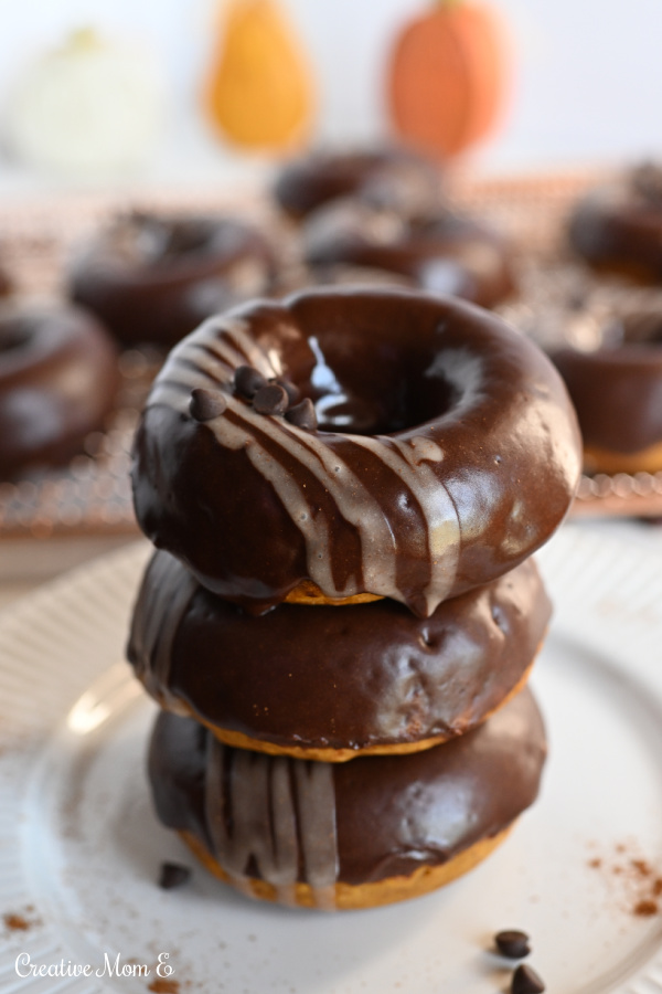 Baked vegan pumpkin donuts in a stack of 3 on a white plate. 